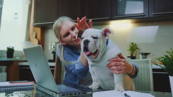 Blonde girl petting bulldog and speaking with it in the kitchen at home - Metraje, vídeo