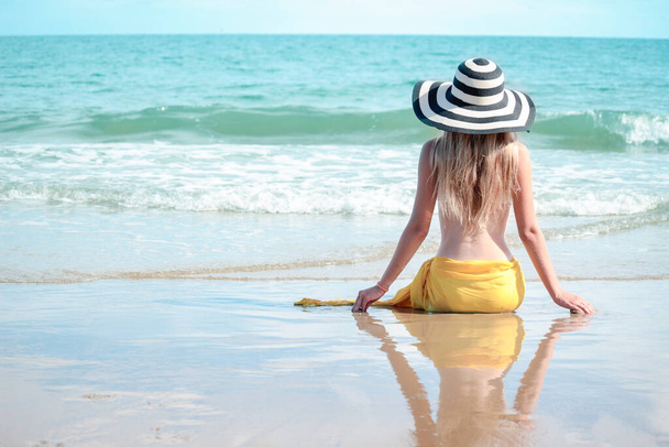 Happy summer holiday vacation, hot sexy beautiful blond women in white bikini and hat with yellow shawl having fun on the beach, resting and spending time to relaxation on tropical island with blue sea - Photo, Image
