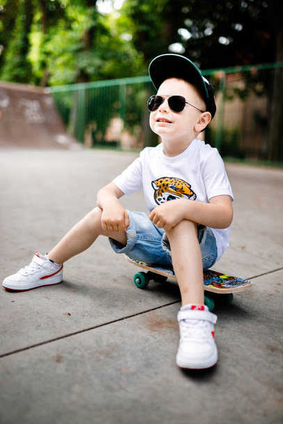 Junge mit Skate in einem Skatepark. Der Junge sitzt auf einem Skateboard. - Foto, Bild