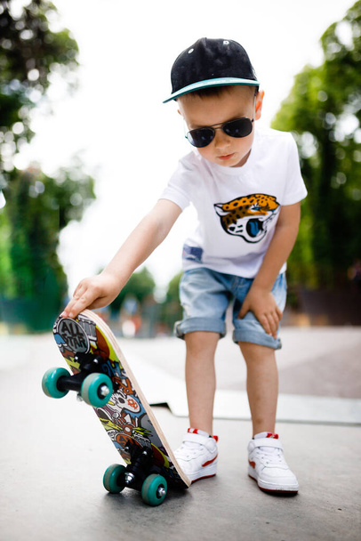 Garçon avec un patin dans un skate park. Un garçon avec des lunettes apprend à patiner. - Photo, image