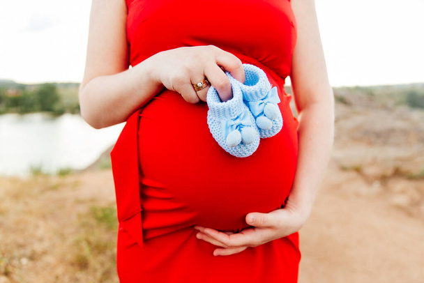 Menina grávida com uma barriga, aguardando o parto, em um vestido vermelho e um chapéu de palha com o marido em um campo e grama de penas
 - Foto, Imagem