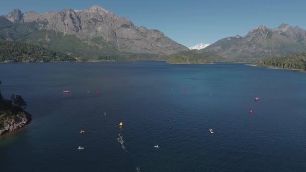 Lucht uitzicht van zwemmers in Ironman triatlon competitie kruising Lake Nahuel Huapi op een zonnige zomerdag. Omgeven door bergen, vegetatie en boten. - Video