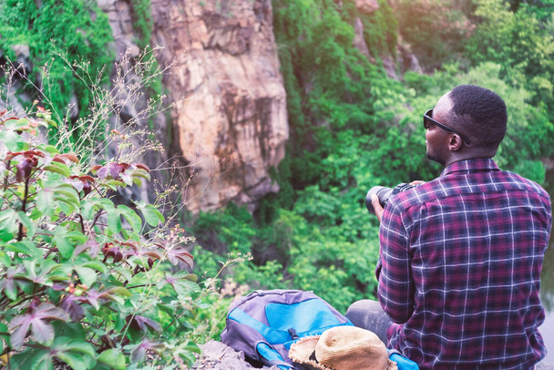 Αφρικανός ταξιδιώτης κάθεται στο γκρεμό και κρατάει την κάμερα - Φωτογραφία, εικόνα