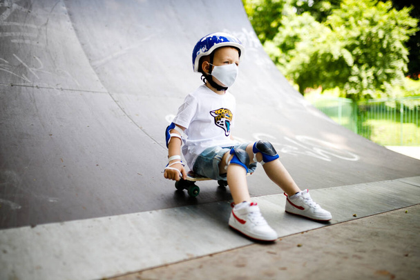 Egy fiú maszkban, korcsolyázni tanul, teljes védelemben a karanténban.. - Fotó, kép