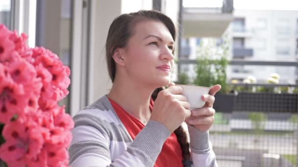 Attractive woman drinks coffee or tea on her home balcony. - Materiaali, video