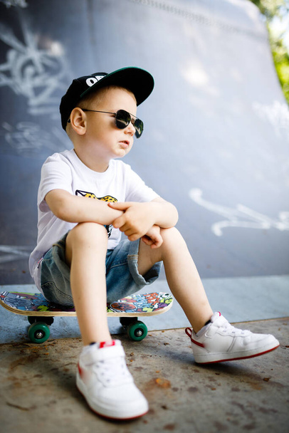 Korcsolyás fiú egy gördeszkás parkban. A fiú egy gördeszkán ül.. - Fotó, kép