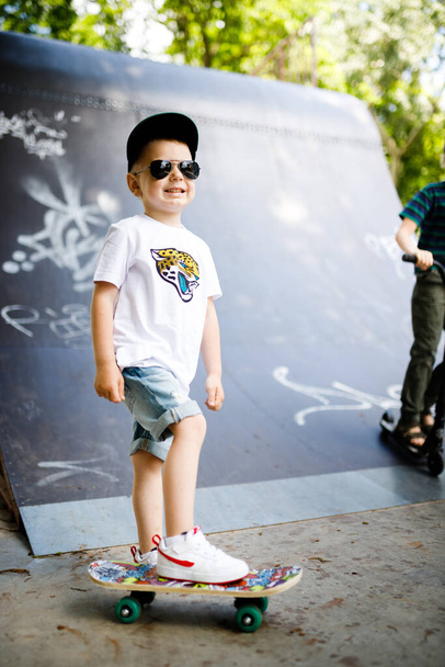 Un chico con un patín en un parque de skate. Un chico con gafas aprende a patinar
. - Foto, Imagen