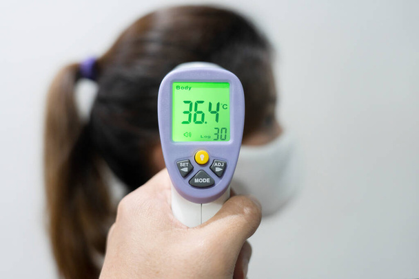 View of Hand Using Electronic Infrared Thermometer Gun Checking Woman Forehead for Body Temperature tp Protect from Corona Virus - Foto, afbeelding