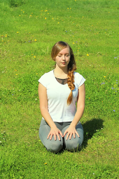 Young woman of European appearance does yoga in summer nature. Woman sitting in hero pose, virasana. High quality photo for web and print with empty space for text and design. - Fotó, kép
