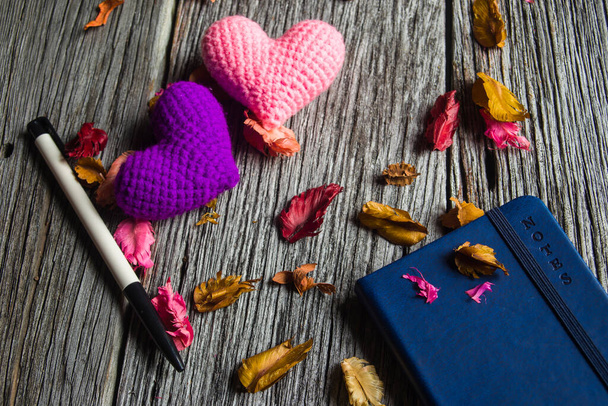 Pink Heart en violet hart en notitieboek met pen op oude houten achtergrond - Foto, afbeelding