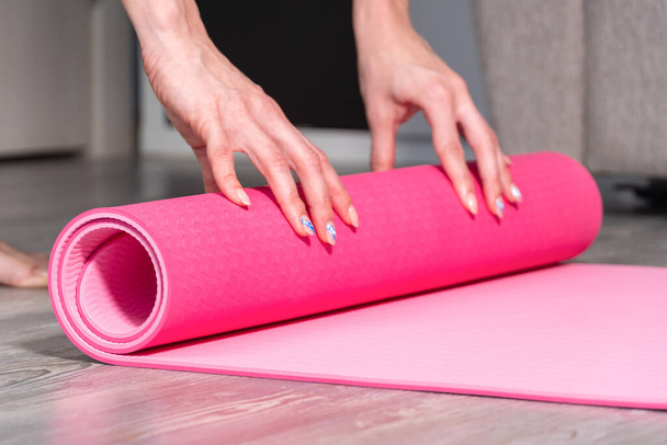 Close-up of attractive young woman folding yoga or fitness mat after working out at home in living room. Healthy life, keep fit concepts - Foto, Bild