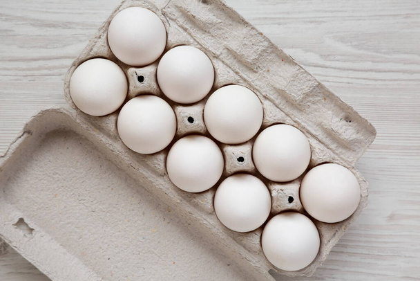 Beyaz ahşap arka planda, kağıt bir kutuda pişmemiş organik beyaz yumurta. Dümdüz, tepeden, yukarıdan. - Fotoğraf, Görsel