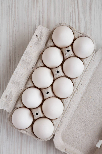 白い木製のテーブルの上の紙箱の中で調理されていない有機白い卵,トップビュー.上から横に寝ろ.  - 写真・画像