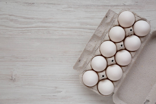 Ongebakken Biologische Witte Eieren in een papieren doos op een wit houten oppervlak, bovenaanzicht. Plat gelegen, boven, van boven. Kopieerruimte. - Foto, afbeelding