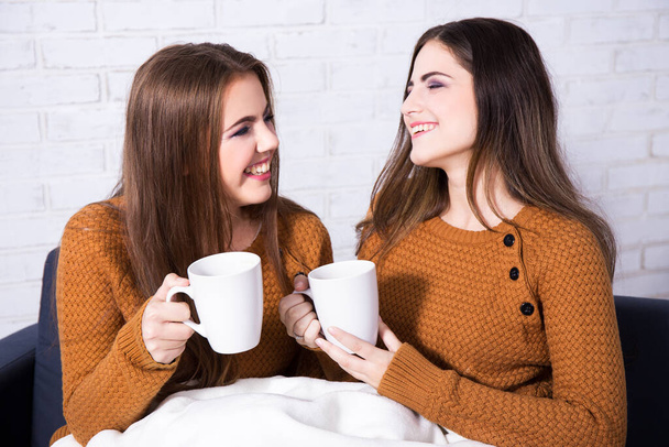 happy friends talking and drinking coffee or tea sitting on sofa at home - Foto, imagen
