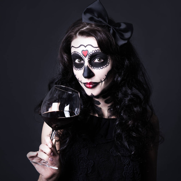 Alkoholabhängiges Konzept - Frau mit Halloween-Totenkopf-Make-up hält Glas Wein oder Blut über schwarzem Hintergrund - Foto, Bild