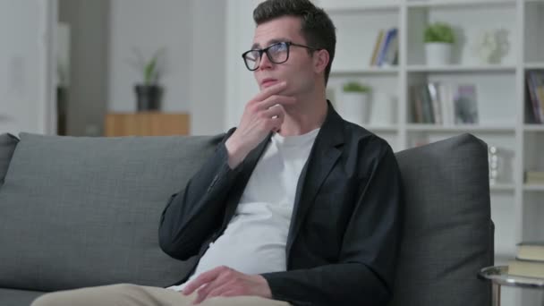 Pensive Young Male Designer Sitting on Sofa and Thinking at Home  - Materiał filmowy, wideo
