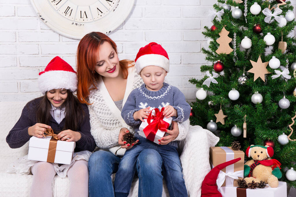 young happy mother and little kids with gift boxes in front of Christmas tree - Photo, Image