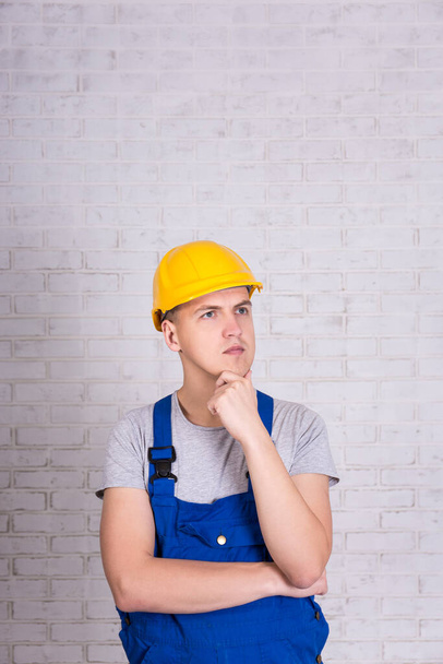 costruttore in uniforme e cappello duro posa su muro di mattoni bianchi - Foto, immagini