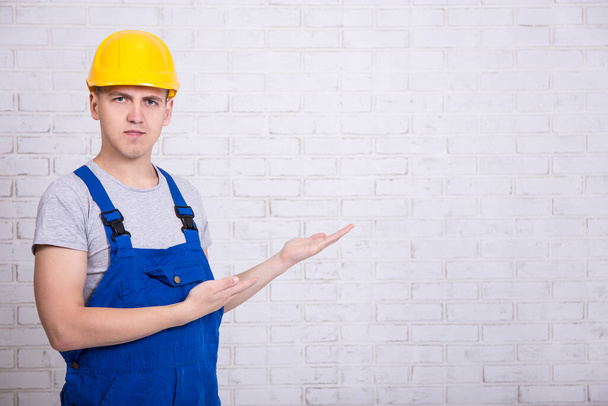 retrato de construtor em uniforme apontando para espaço de cópia sobre parede de tijolo branco
 - Foto, Imagem