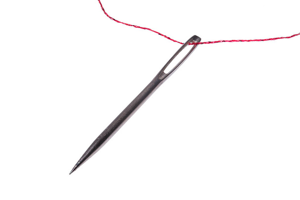 Vista muy detallada de una aguja de coser y un hilo rojizo aislados sobre un fondo blanco
 - Foto, imagen