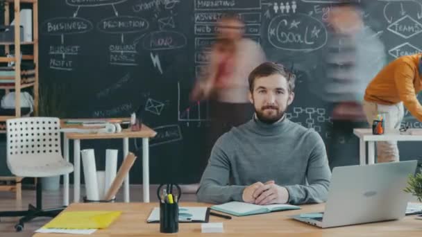 Time lapse portrait of ambitious man at desk in open space office with people working around - Séquence, vidéo