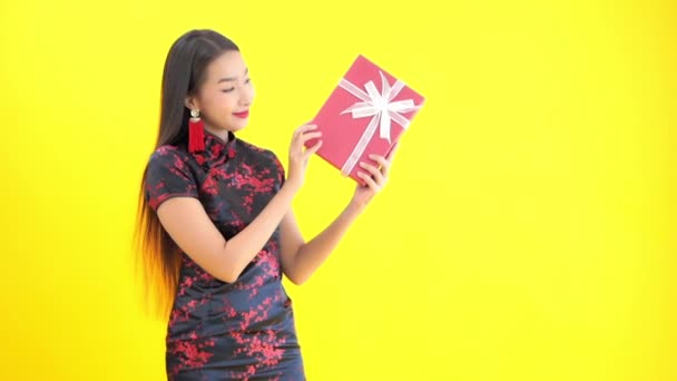 close-up footage of beautiful young Asian woman in traditional chinese dress with pink gift box isolated on yellow - Metraje, vídeo