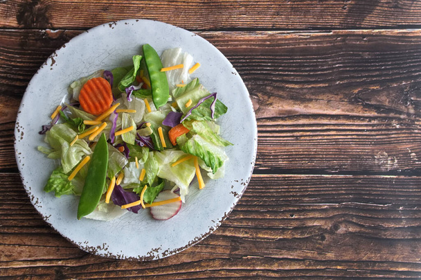 Μια ανάμεικτη σαλάτα λαχανικών σε στρογγυλό άσπρο πιάτο σε ξύλινο φόντο, με λίγο χώρο αντιγραφής στα δεξιά - Φωτογραφία, εικόνα