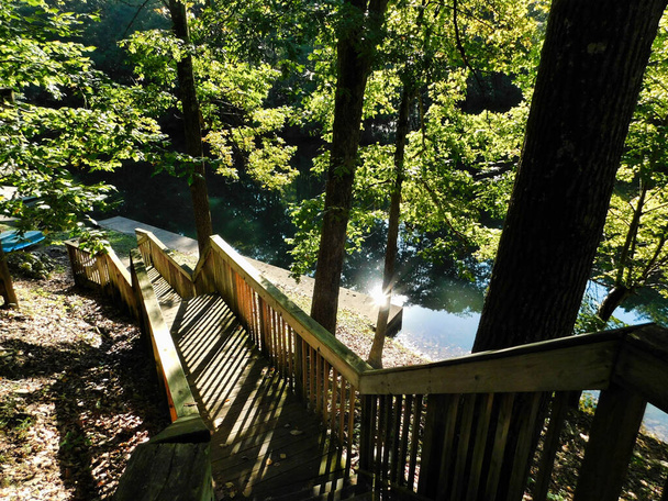 Вид вниз по лестнице к причалу на берегу озера, с утренним солнцем вне воды, в лагере Blue Mountain в Гамбурге, штат Пенсильвания
 - Фото, изображение
