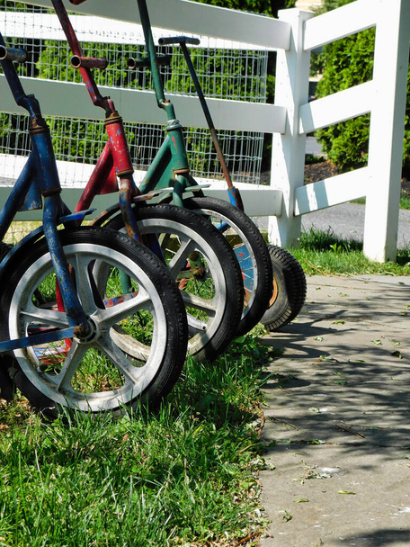 Perspectiva única das rodas e scooters de crianças Amish, esperando pela cerca fora da escola
 - Foto, Imagem
