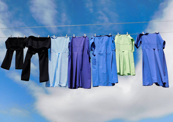 手作りのアーミッシュドレスと黒のパンツは、風の中で服のラインで乾燥し、背景に青い空と雲があります。 - 写真・画像