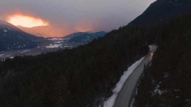 DRONE: Помаранчевий захід сонця освітлює ліс, коли автомобіль їде по мальовничому шосе
 - Кадри, відео