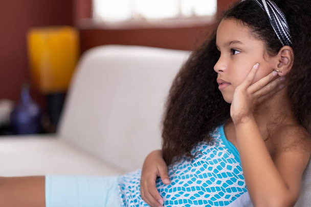 χαριτωμένο πολυφυλετικό μικρό κορίτσι με όμορφα σγουρά μαλλιά βλέποντας τηλεόραση στο σπίτι - Φωτογραφία, εικόνα