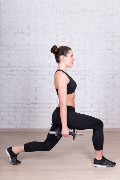 young slim woman doing exercises with dumbbells over white brick wall background - Foto, afbeelding