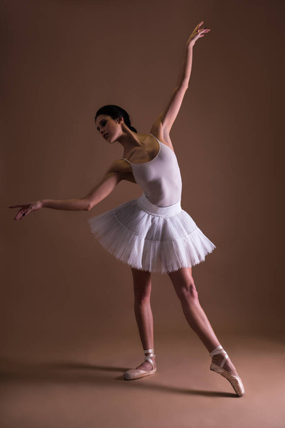 Tutulu güzel kadın balerin bej arka planda ayak parmaklarıyla poz veriyor. - Fotoğraf, Görsel