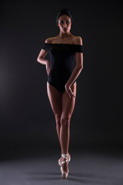 όμορφη γυναίκα μπαλαρίνα σε μαύρο κοστούμι του σώματος ποζάρουν στα δάχτυλα των ποδιών πάνω από το μαύρο φόντο - Φωτογραφία, εικόνα