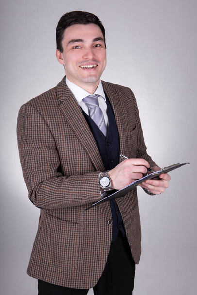 happy young business man writing something on clipboard over grey background - Photo, image