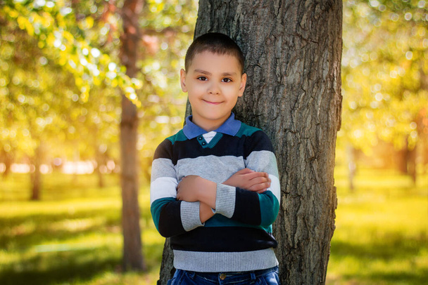 Хлопчик стоїть, спираючись на дерево в парку
. - Фото, зображення