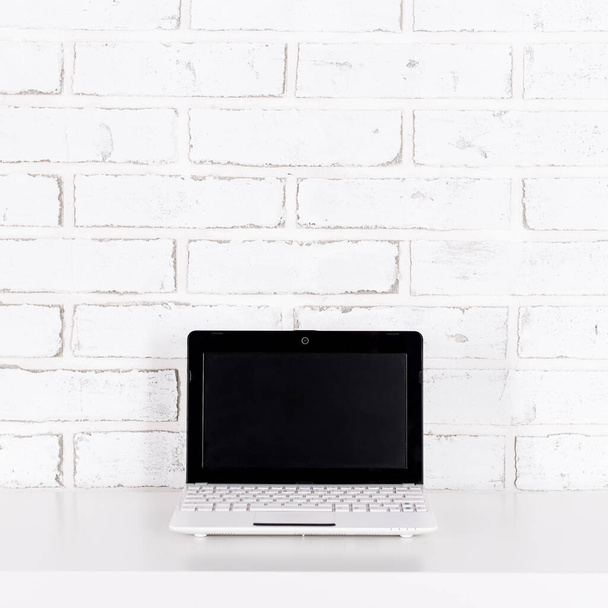 computer portatile moderno con schermo bianco sul tavolo su sfondo muro di mattoni bianchi - Foto, immagini