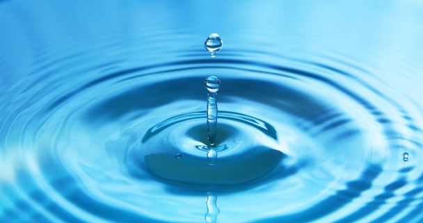 Vízcsepp esik a vízbe, így tökéletes koncentrikus körök. Absztrakt kék háttér. - Fotó, kép