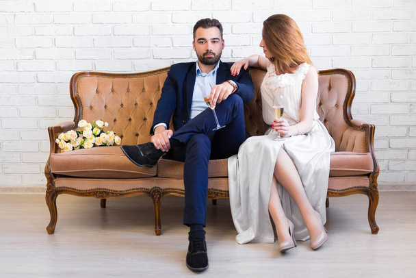 happy beautiful couple with glasses of champagne sitting on vintage sofa - Photo, Image