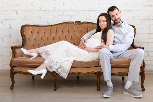 joven hermosa embarazada pareja sentado en vintage sofá en casa
 - Foto, imagen