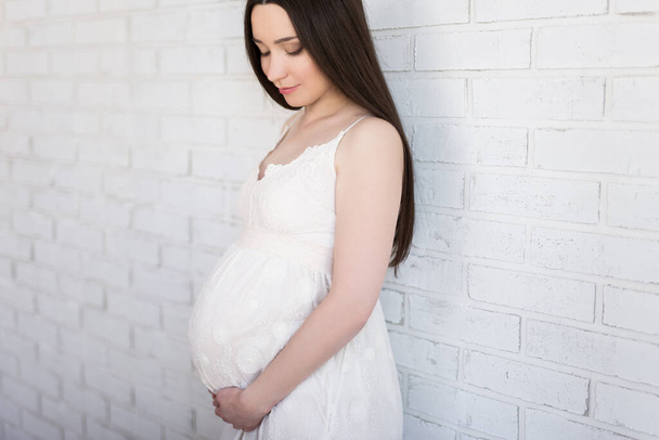 εγκυμοσύνη και μητρότητα έννοια - πορτρέτο της όμορφης εγκύου γυναίκα θέτει πάνω από λευκό τοίχο τούβλο - Φωτογραφία, εικόνα