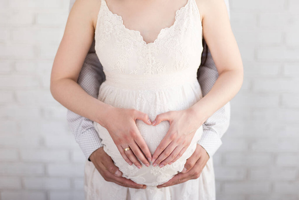 έννοια της εγκυμοσύνης - ζευγάρι κάνει ένα σχήμα καρδιάς με τα χέρια τους στην κοιλιά έγκυος - Φωτογραφία, εικόνα