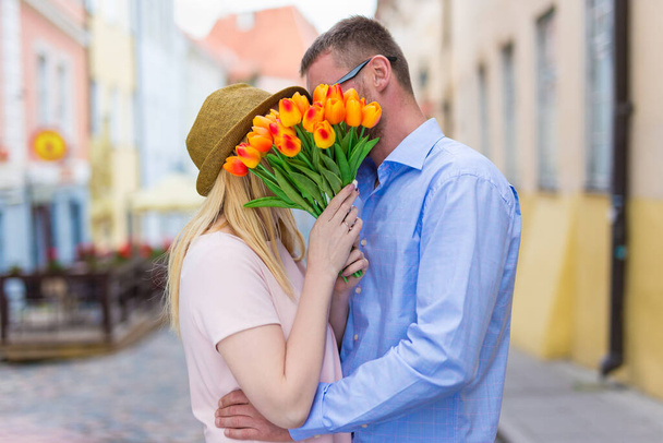 szerelem és kapcsolat koncepció - fiatal pár csók a városban virágokkal - Fotó, kép