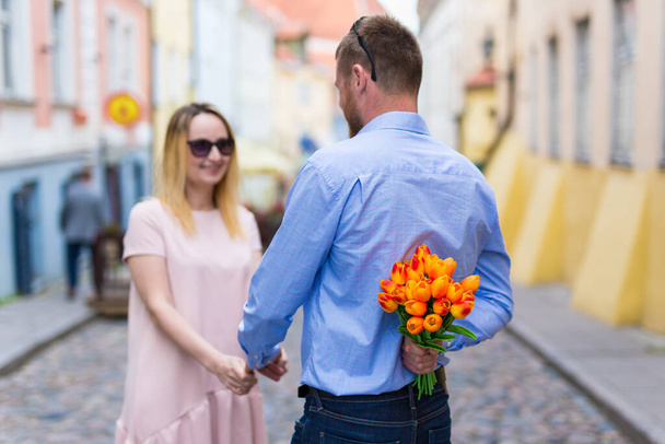 love and relationship concept - young man giving flowers to his girlfriend in the city - Photo, Image