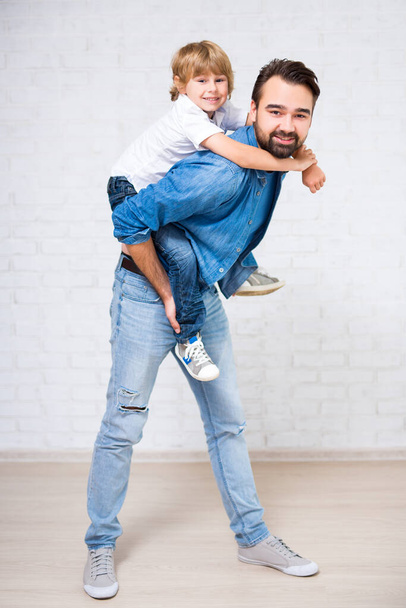 glückliches Familienporträt - Vater mit niedlichem kleinen Sohn über weißer Ziegelwand - Foto, Bild