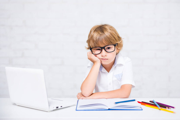annoiato piccolo ragazzo della scuola in occhiali facendo i compiti a casa - Foto, immagini
