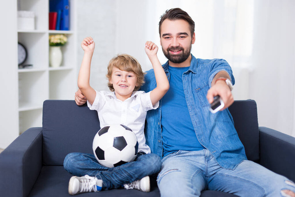 Mutlu genç baba ve oğul televizyonda futbol seyrediyor. - Fotoğraf, Görsel