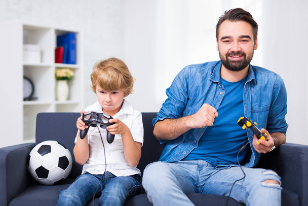 ganador y perdedor - padre joven e hijo con gamepads jugando videojuego en casa
 - Foto, imagen